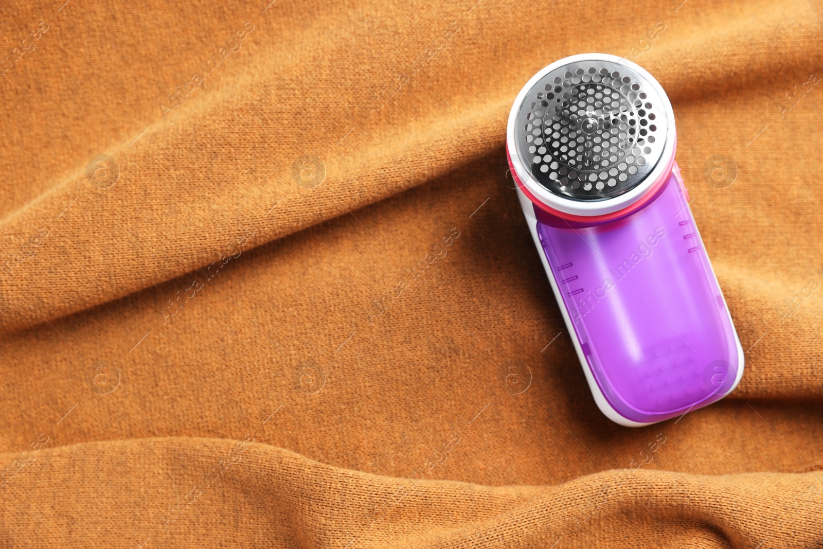 Photo of Modern fabric shaver on brown cloth, top view. Space for text