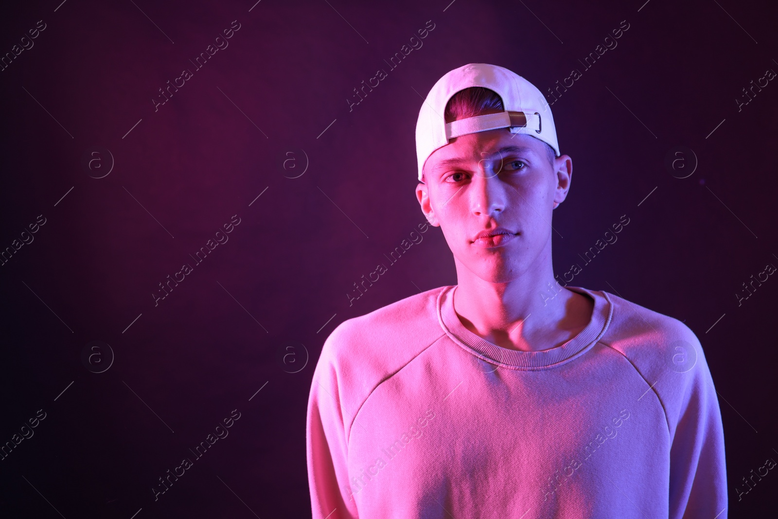 Photo of Young man on dark background in neon light. Space for text