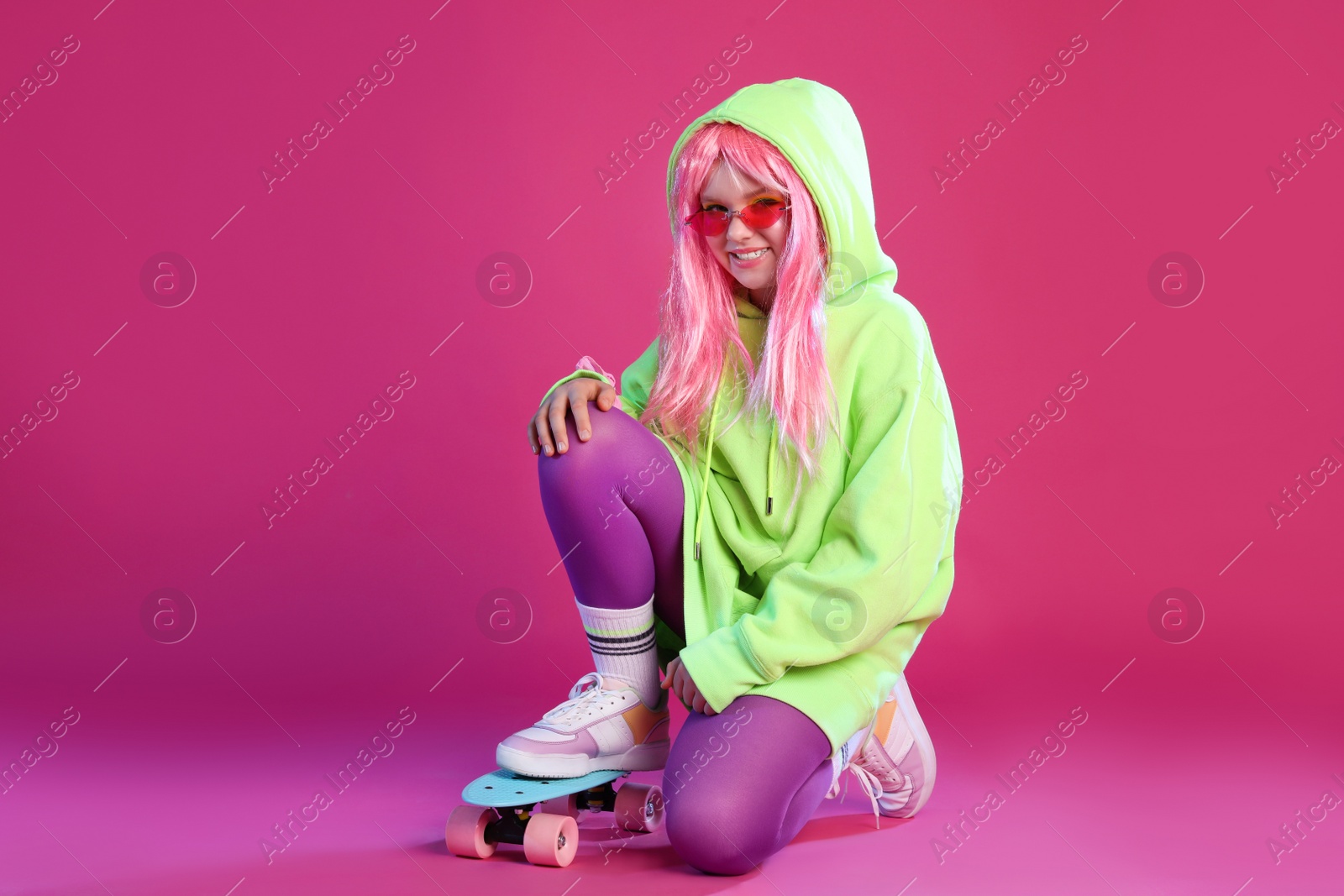 Photo of Cute indie girl with sunglasses and penny board on violet background