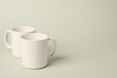 Two white ceramic mugs on light grey background, space for text