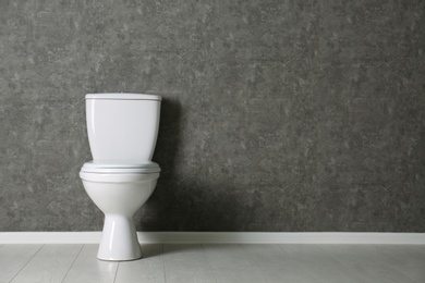 Photo of New toilet bowl near grey wall indoors. Space for text
