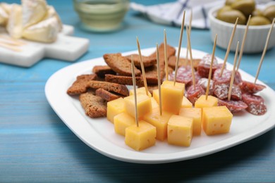 Photo of Toothpick appetizers. Pieces of sausage, cheese and croutons on light blue wooden table, closeup