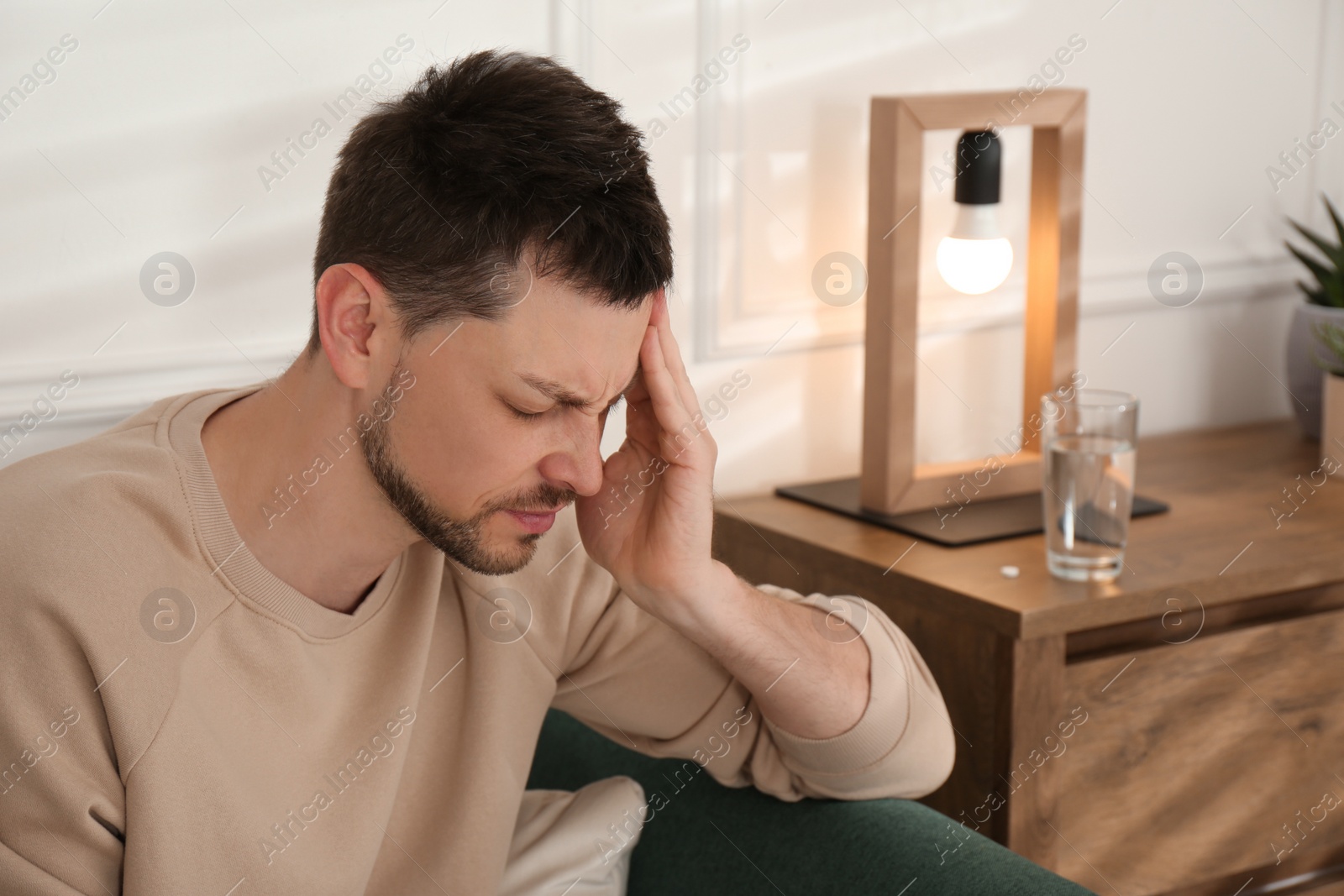 Photo of Man suffering from terrible migraine on sofa at home