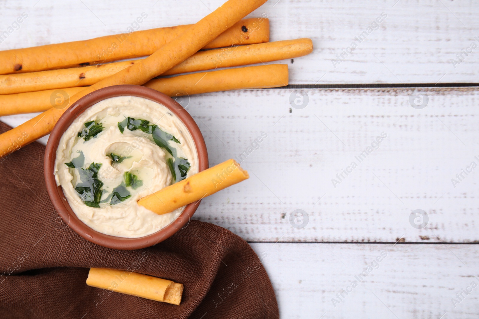 Photo of Delicious hummus with grissini sticks on white wooden table, flat lay. Space for text