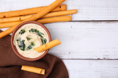 Photo of Delicious hummus with grissini sticks on white wooden table, flat lay. Space for text