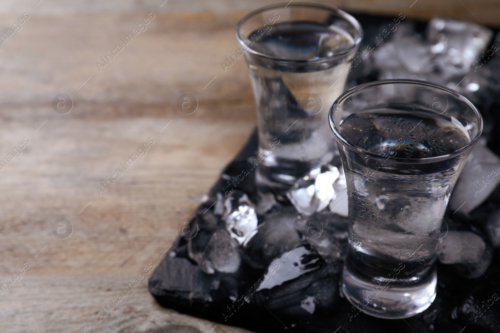 Photo of Vodka in shot glasses and ice on wooden table, space for text