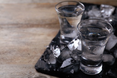 Vodka in shot glasses and ice on wooden table, space for text