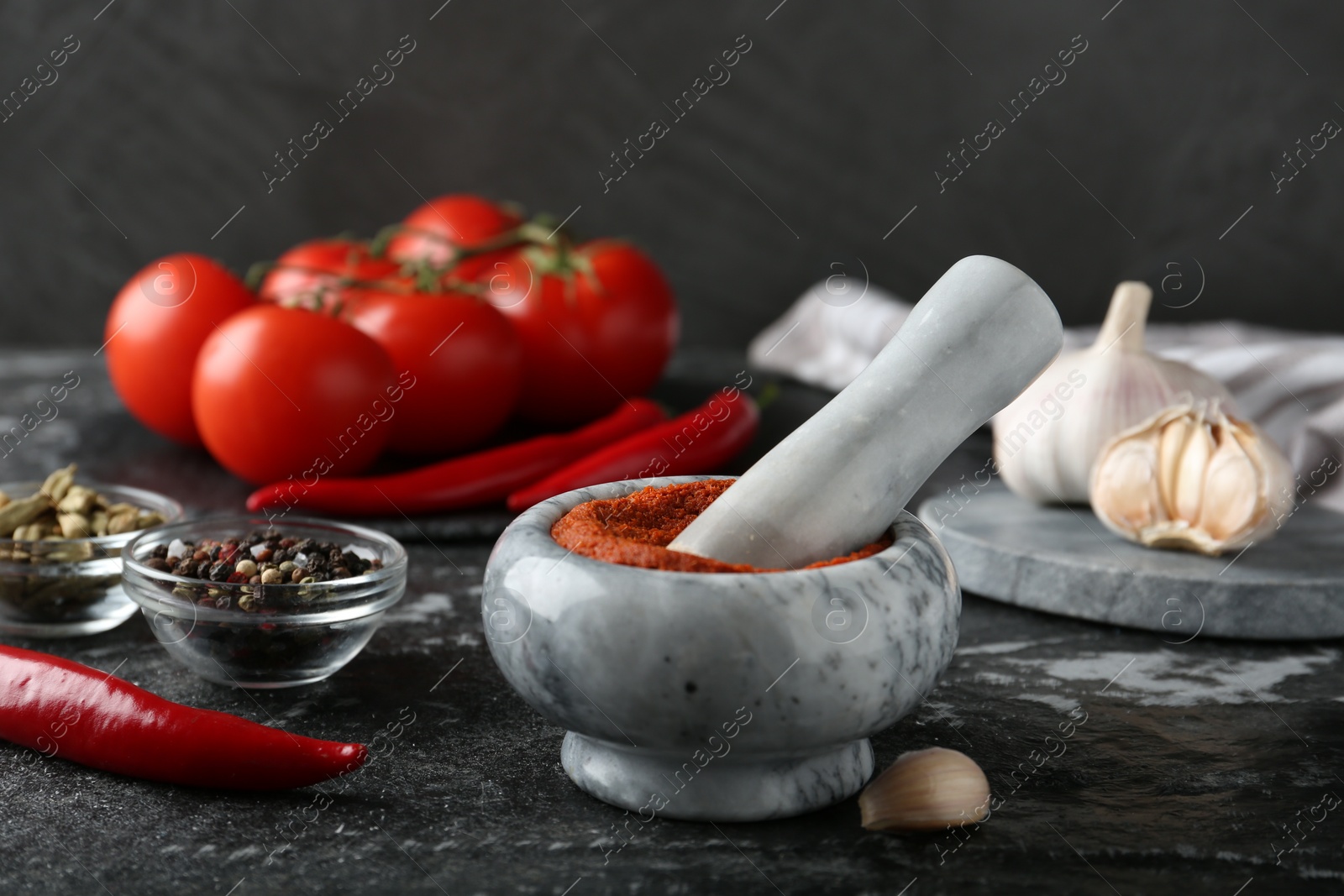 Photo of Mortar with red curry paste and ingredients on black textured table