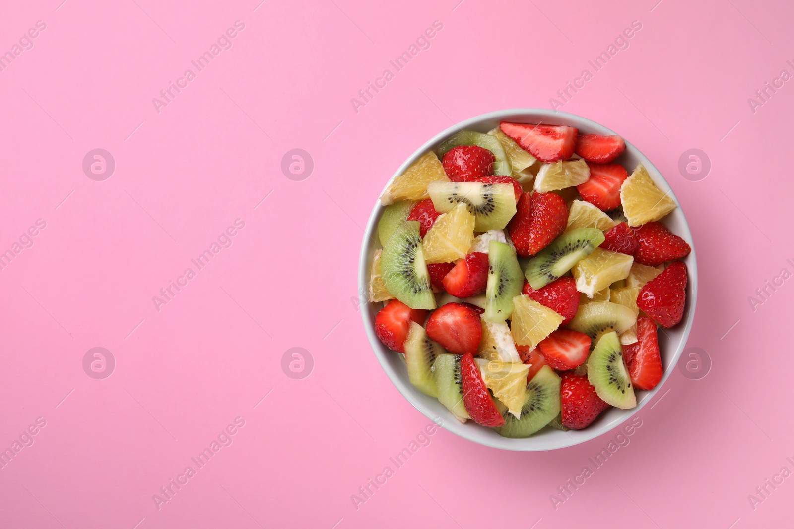 Photo of Yummy fruit salad in bowl on pink background, top view. Space for text