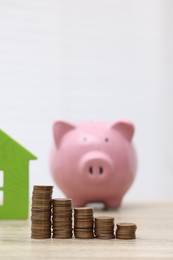 Photo of House model, piggy bank and stacked coins on wooden table, selective focus