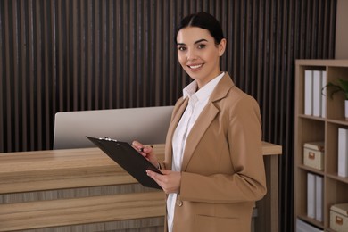 Receptionist with clipboard near countertop in office, space for text