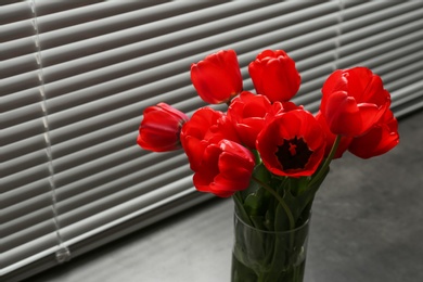 Photo of Bouquet of beautiful tulips in vase near window with blinds