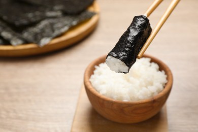 Chopsticks with cooked rice wrapped in nori sheet over table, closeup. Space for text