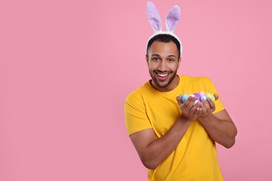 Photo of Happy African American man in bunny ears headband with Easter eggs on pink background, space for text