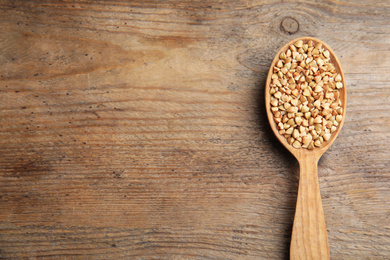 Photo of Spoon with green buckwheat on wooden table, top view. Space for text