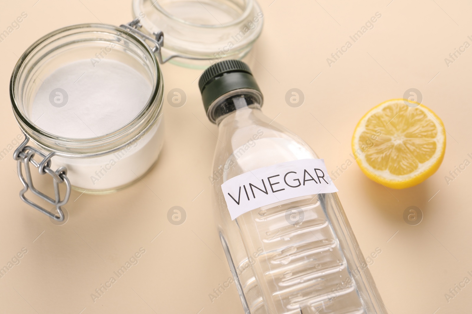 Photo of Eco friendly natural cleaners. Vinegar in bottle, cut lemon and jar of soda on beige background