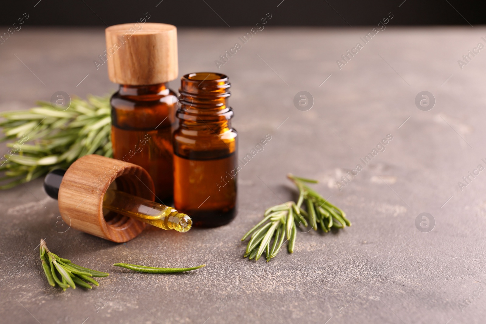 Photo of Essential oil in bottles, dropper and rosemary on grey table