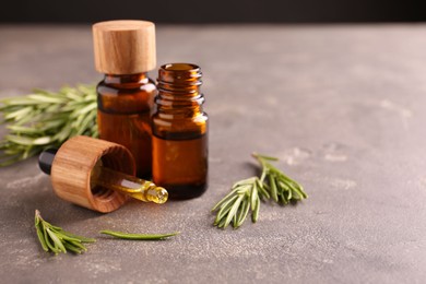 Photo of Essential oil in bottles, dropper and rosemary on grey table