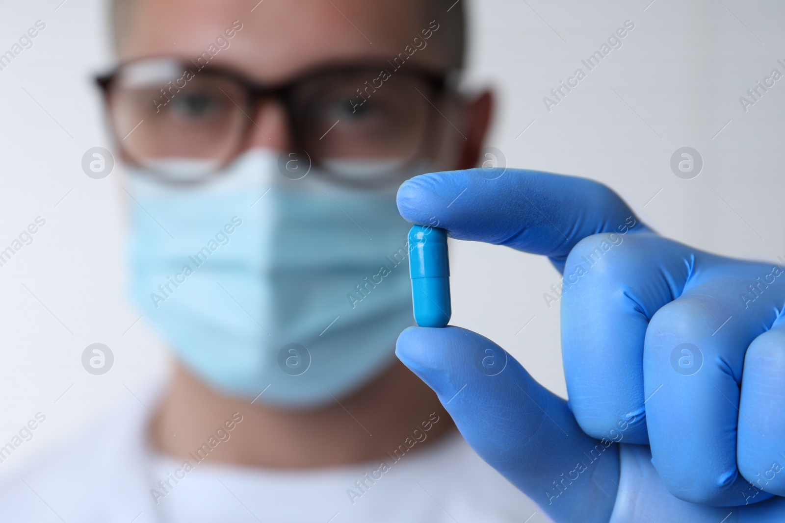 Photo of Doctor holding pill on light background, selective focus. Space for text