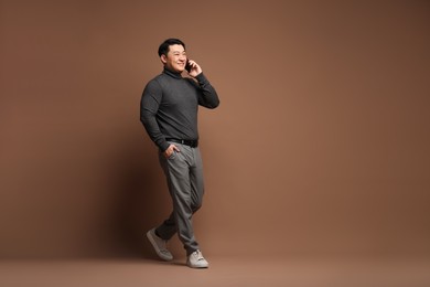 Full length portrait of happy man talking by smartphone on brown background. Space for text