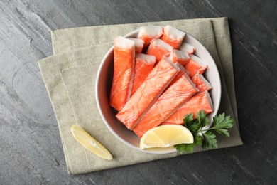 Photo of Crab sticks with lemon in bowl on grey table, flat lay