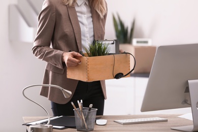 Photo of Young woman holding moving box with office stuff indoors, closeup