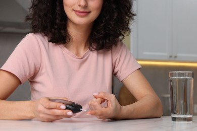 Photo of Diabetes. Woman checking blood sugar level with glucometer at table in kitchen, closeup