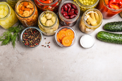 Glass jars with different pickled vegetables on grey table, flat lay. Space for text