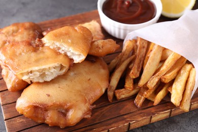 Photo of Tasty fish, chips and sauce on grey table, closeup