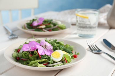 Photo of Fresh spring salad with flowers served on white wooden table