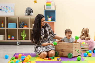 Young nanny and cute little baby playing with toys at home