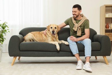 Happy man sitting on sofa with his cute Labrador Retriever at home