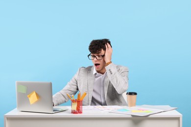 Photo of Emotional young man working at white table on light blue background. Deadline concept