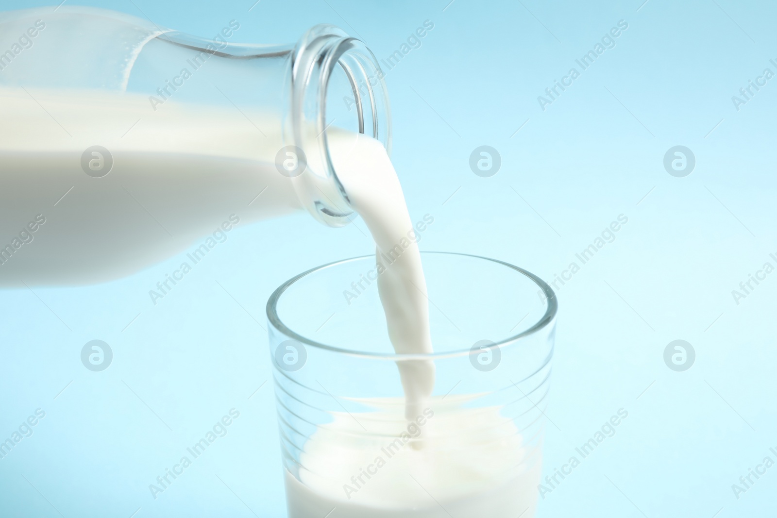 Photo of Pouring milk into glass on light blue background, closeup