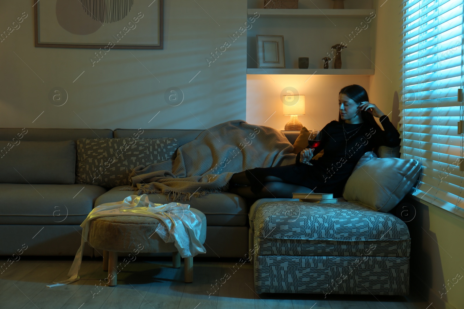 Photo of Woman with glass of wine resting on couch in room at night