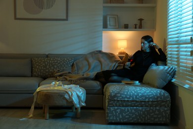 Woman with glass of wine resting on couch in room at night