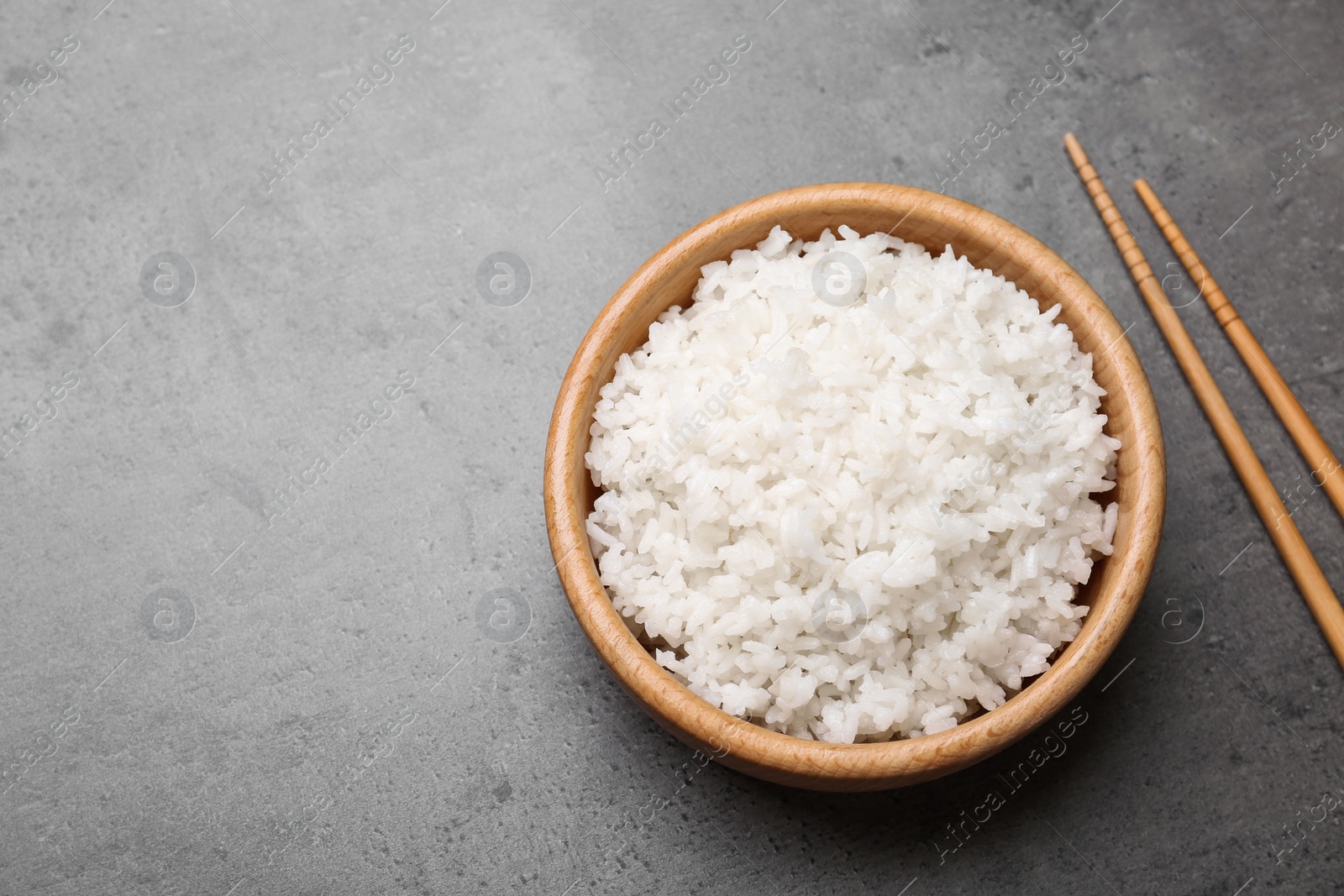 Photo of Flat lay composition of bowl of boiled rice with chopsticks on table. Space for text