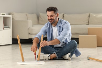 Man with screwdriver assembling table on floor at home