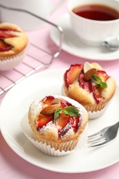 Photo of Delicious cupcakes with plums on pink wooden table