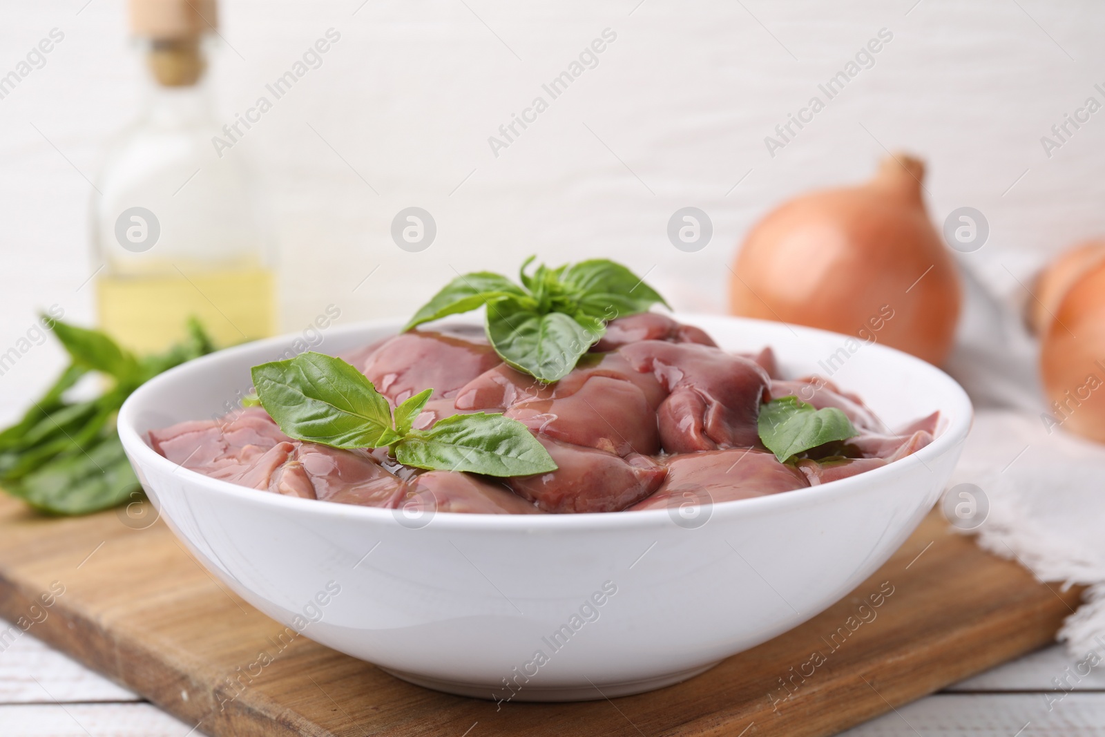 Photo of Bowl with raw chicken liver and basil on white wooden table