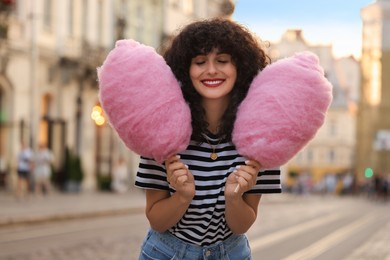 Portrait of happy woman with pink cotton candies on city street