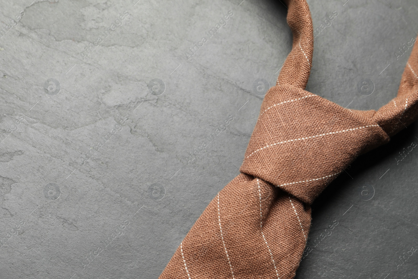 Photo of One striped necktie on grey textured table, top view. Space for text