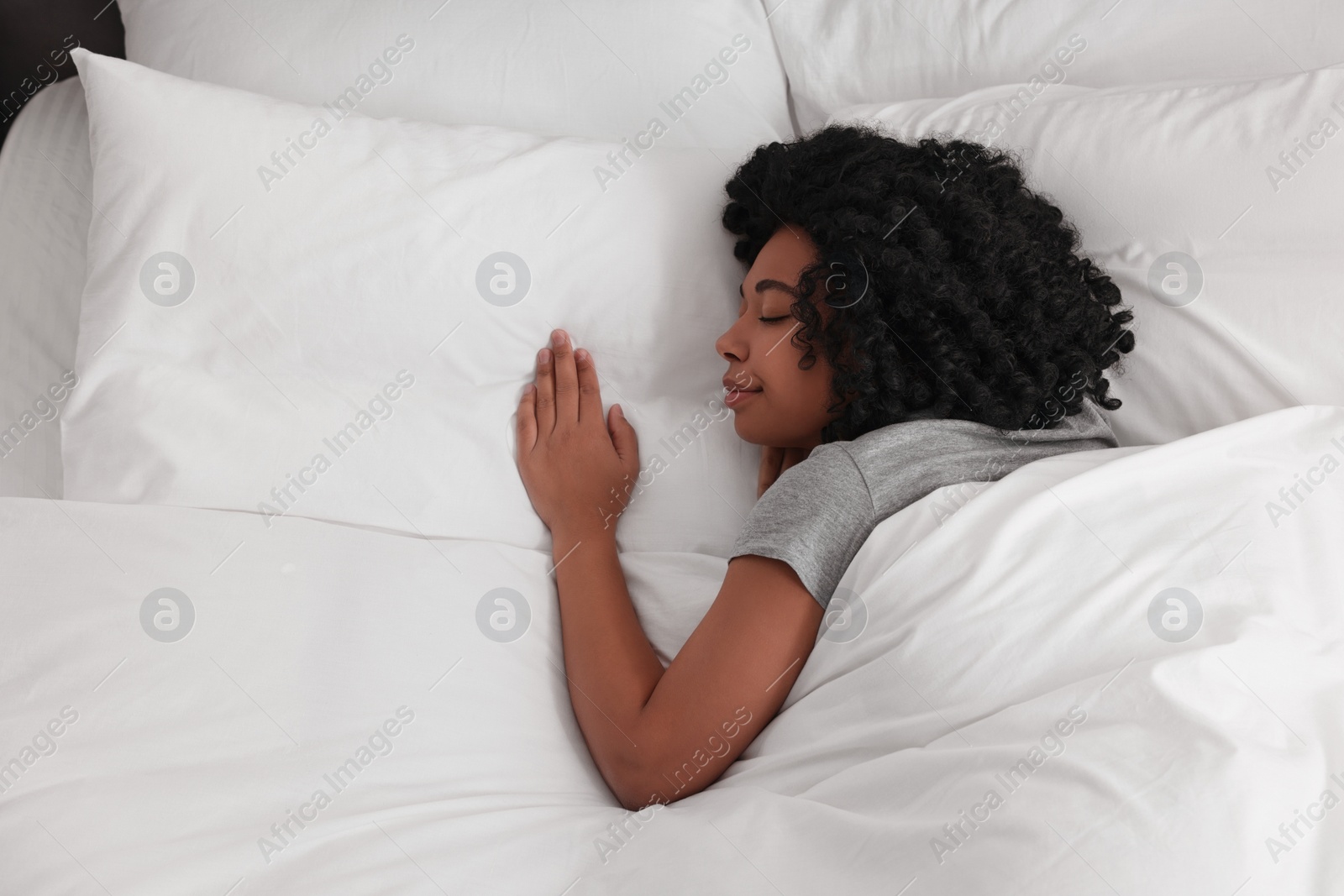 Photo of Beautiful young woman sleeping in soft bed, top view