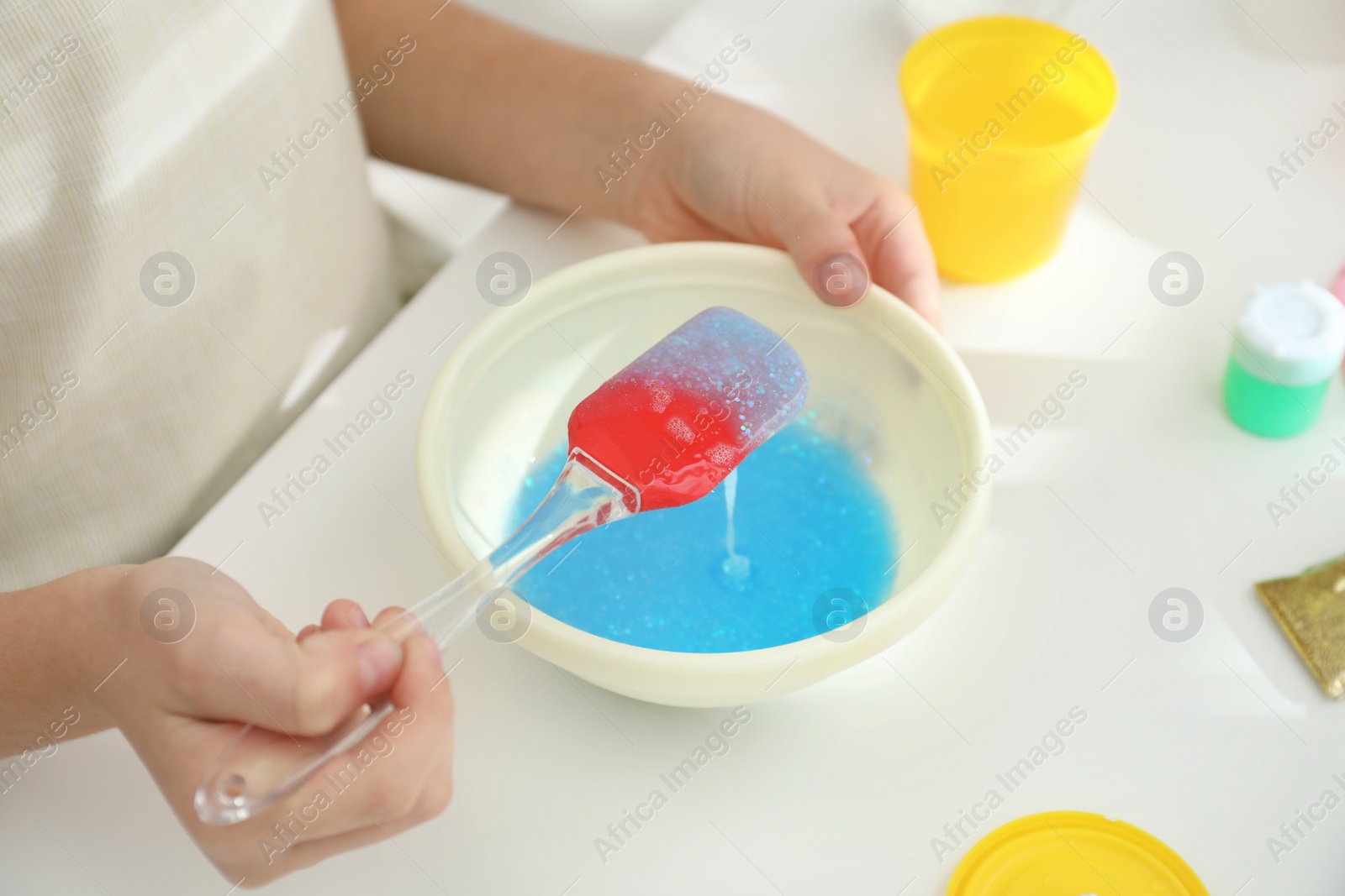 Photo of Little girl mixing ingredients with silicone spatula at table, closeup. DIY slime toy