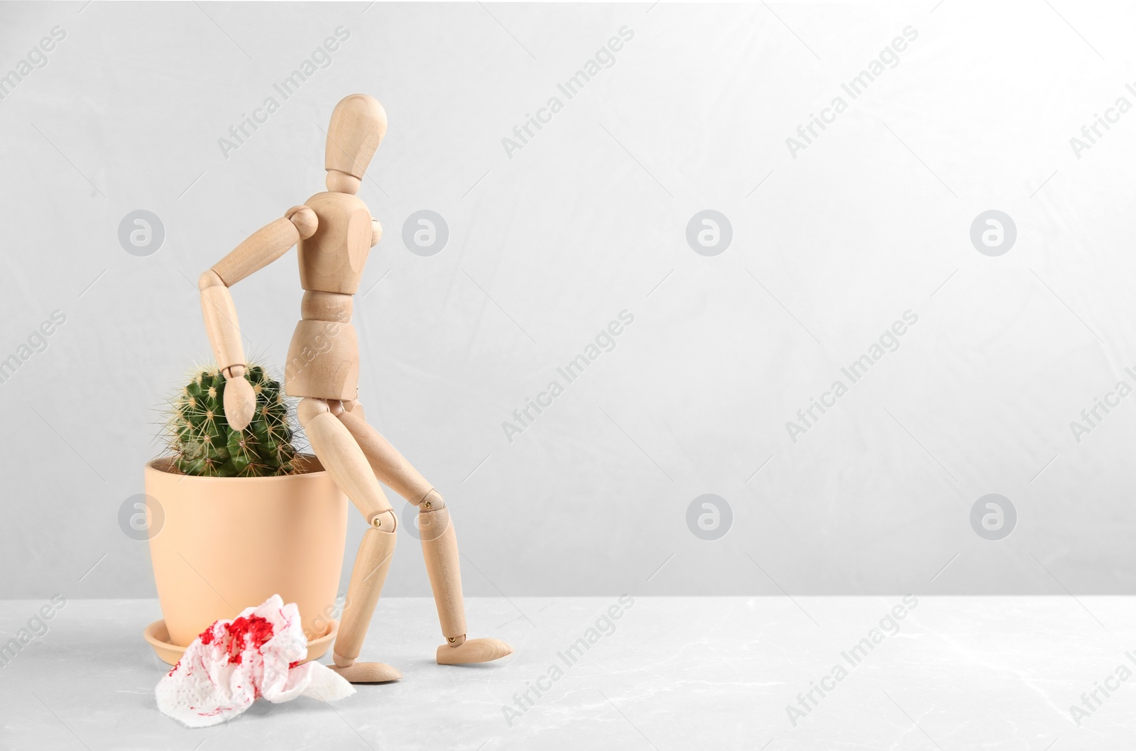 Photo of Wooden human figure, cactus and sheet of toilet paper with blood on table, space for text. Hemorrhoid problems