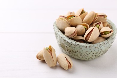 Photo of Delicious pistachios in bowl on white table, closeup. Space for text