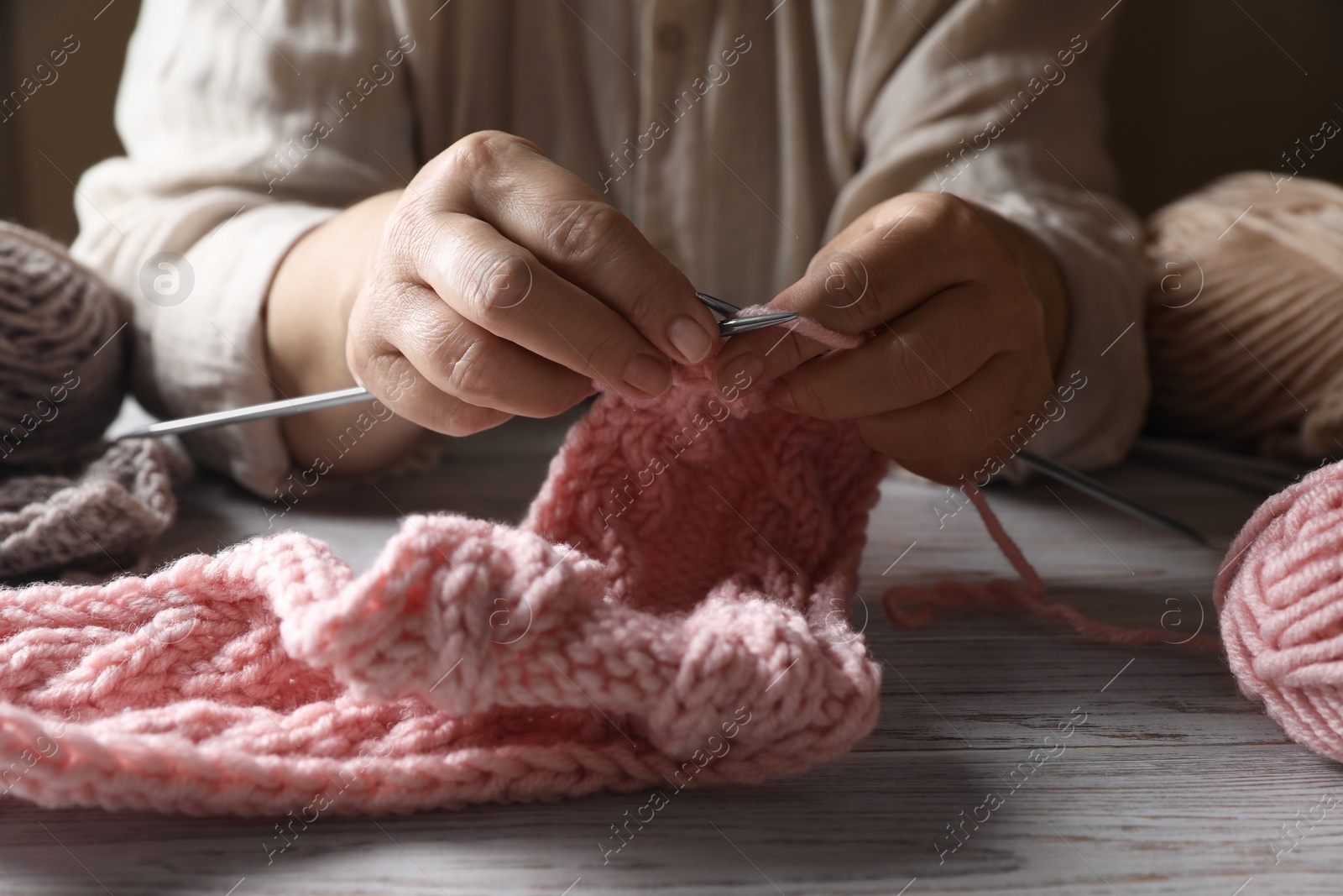 Photo of Woman knitting at white wooden table, closeup. Creative hobby