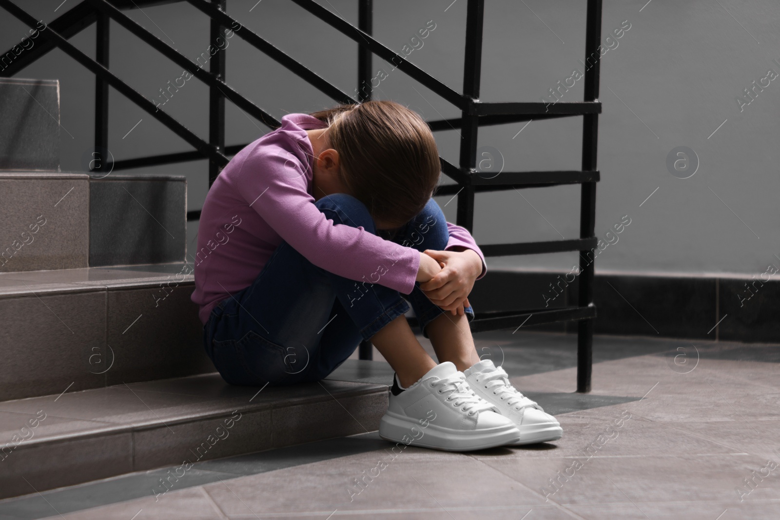 Photo of Child abuse. Upset girl sitting on stairs