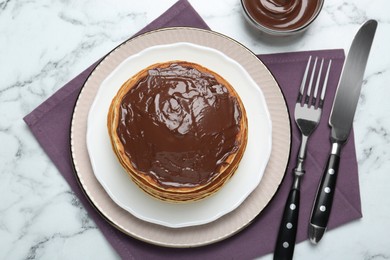 Photo of Tasty pancakes with chocolate paste and cutlery on white marble table, flat lay