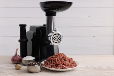 Photo of Electric meat grinder with beef mince, spices and garlic on white wooden table, space for text